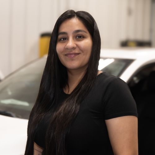Woman in black shirt smiling in front of a silver car.