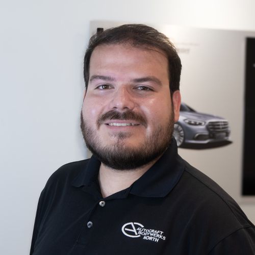 Smiling man in a black polo shirt standing indoors, with a car poster in the background
