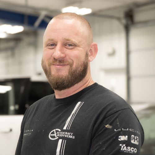 Smiling bald man with a beard in a black shirt standing in a workshop.