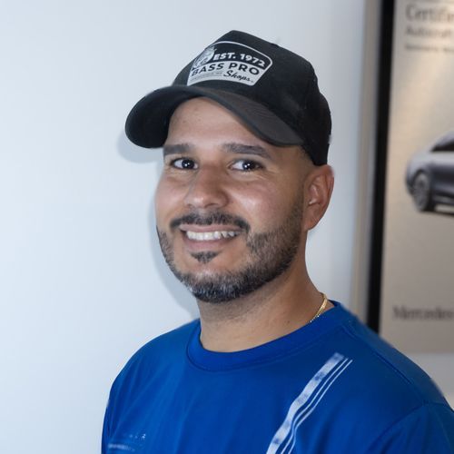 Smiling man in a blue shirt and black cap standing indoors near a wall poster