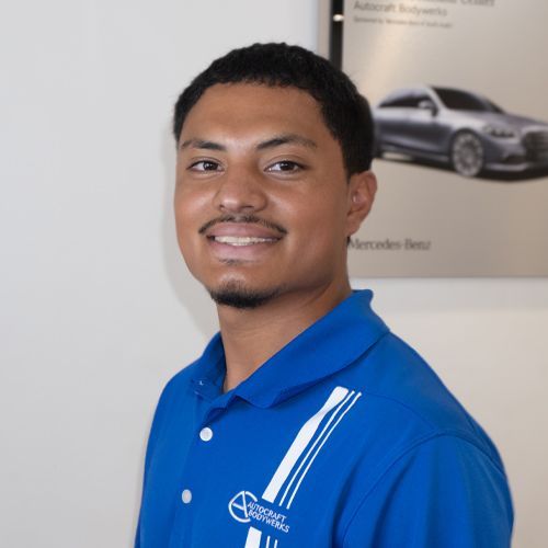 Man in a blue polo smiling in an office, with a car poster in the background
