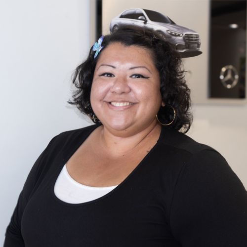 Smiling woman in black top standing indoors with a toy car on her head