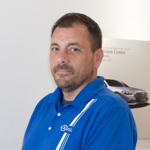 Man in blue polo shirt standing indoors in front of a white wall and car poster