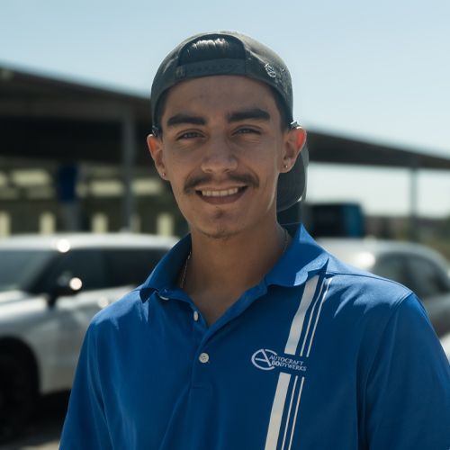 Smiling man in a blue polo shirt and backward cap standing outdoors by parked cars