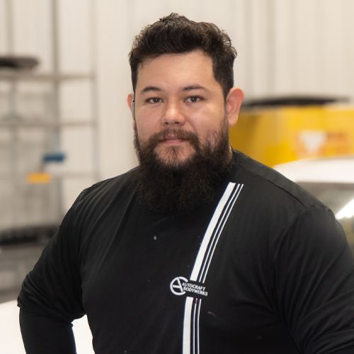 Man in black shirt with white stripes standing indoors against a blurred industrial background