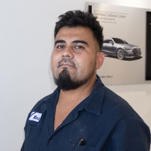 Man in a navy work shirt standing indoors near a wall poster with a car image