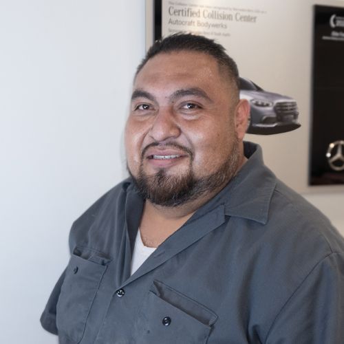 Smiling man in gray shirt standing in an auto service showroom with car posters behind him