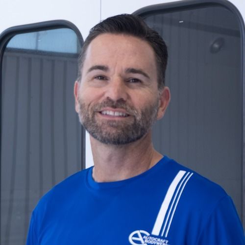 Smiling man in a blue shirt standing in front of a boat