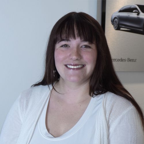 Smiling person in white top standing before a Mercedes-Benz display poster