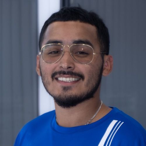 Smiling person with glasses wearing a blue shirt against a gray background