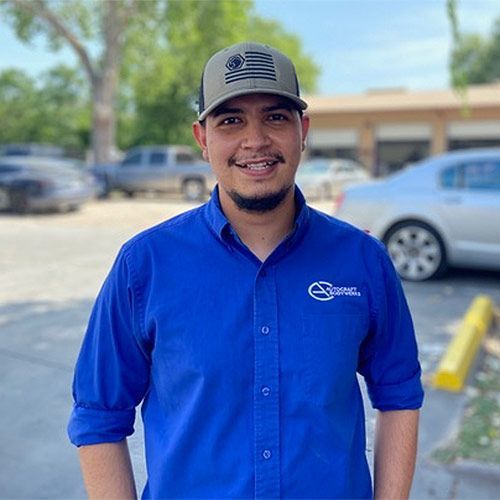 Man wearing a blue shirt and a cap, smiling outside a building.