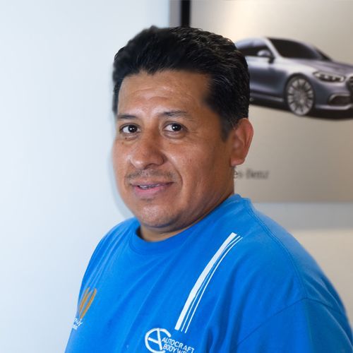 Man in blue shirt standing indoors with a car poster on the wall behind him
