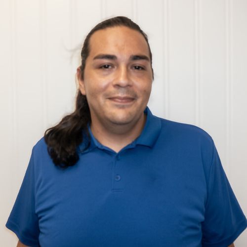 Person in a blue polo shirt smiling against a light wall.