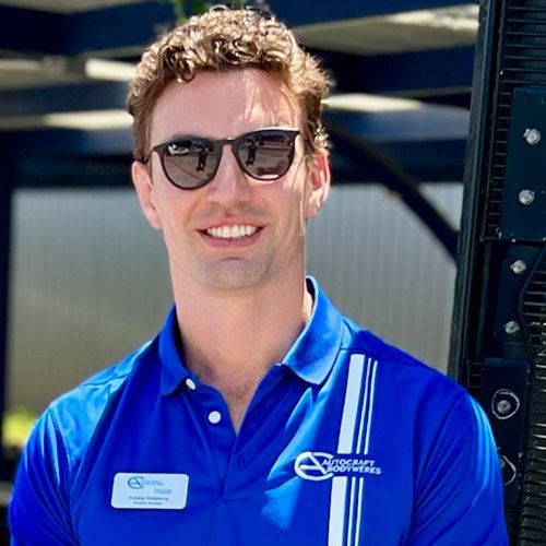Man wearing sunglasses and blue polo shirt with company logo, smiling outdoors.