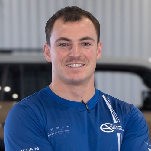 Smiling man in a blue shirt standing in a garage or workshop