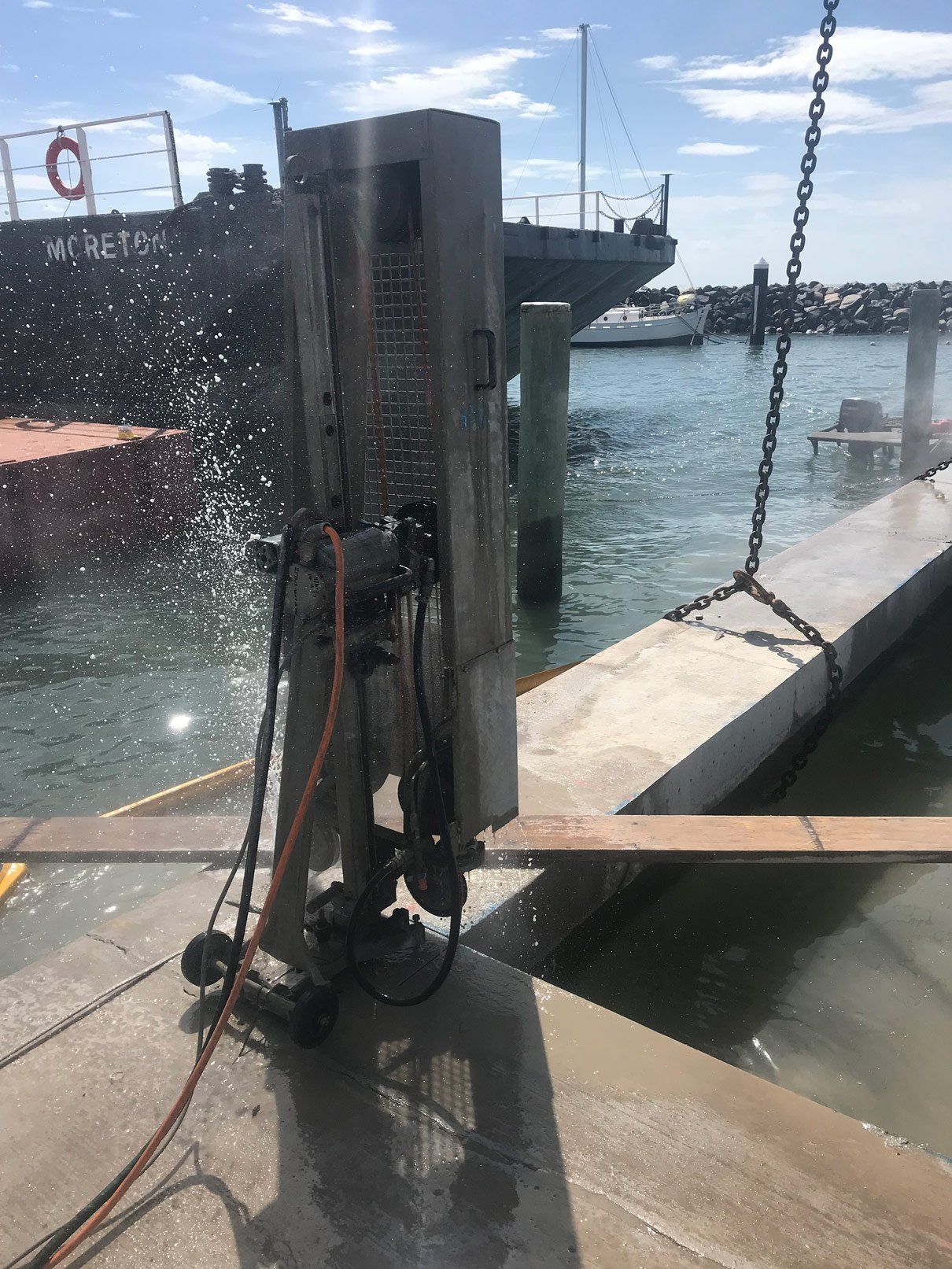 A machine is cutting a concrete dock next to a body of water.