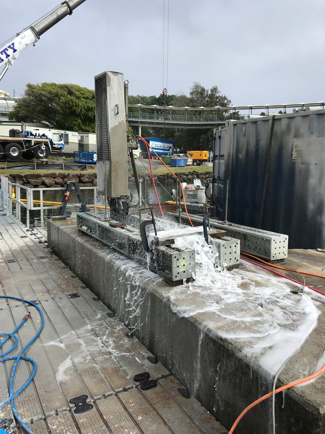 A machine is cutting a concrete wall with a crane in the background.