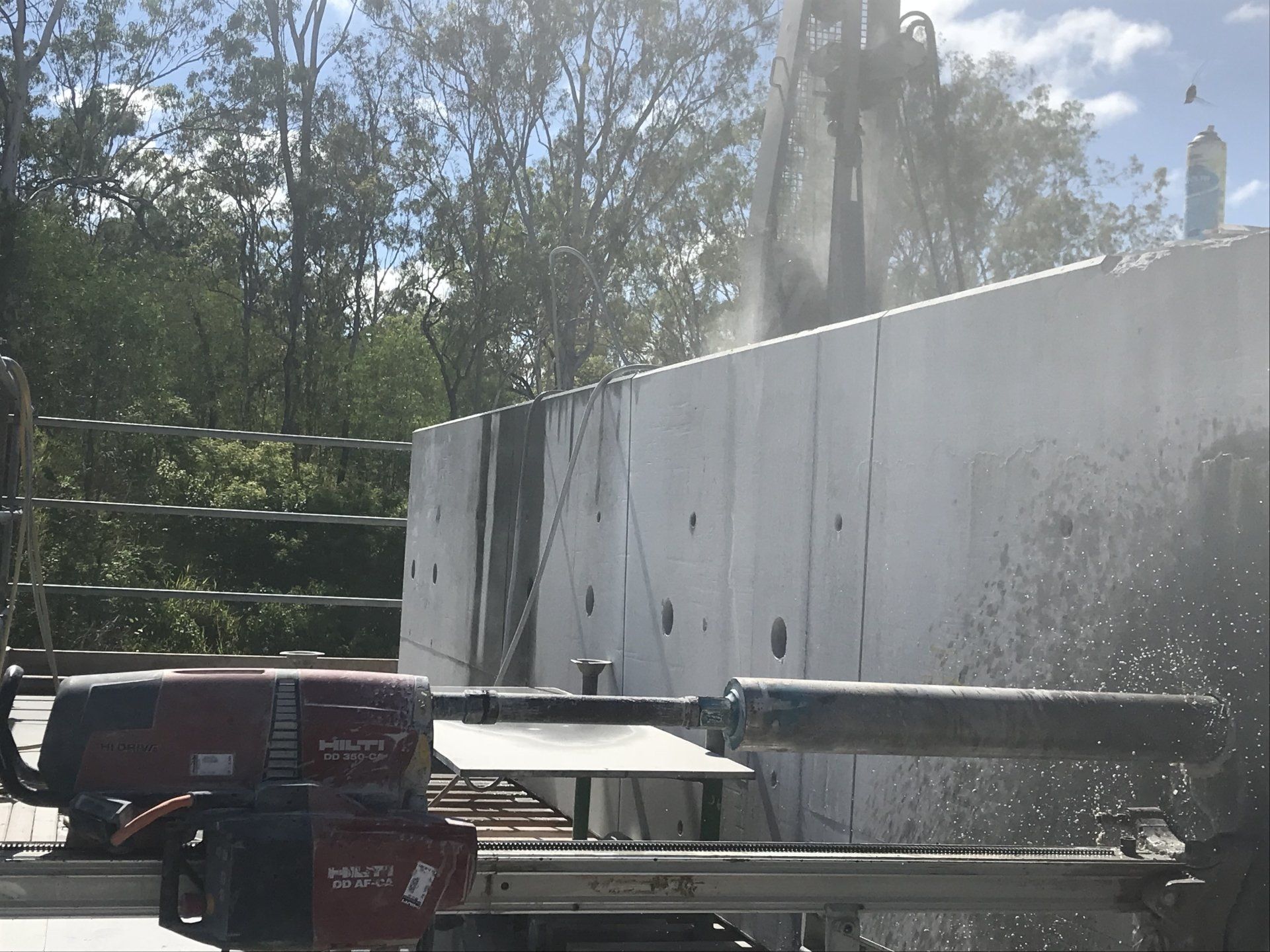 A machine is cutting a concrete wall with trees in the background