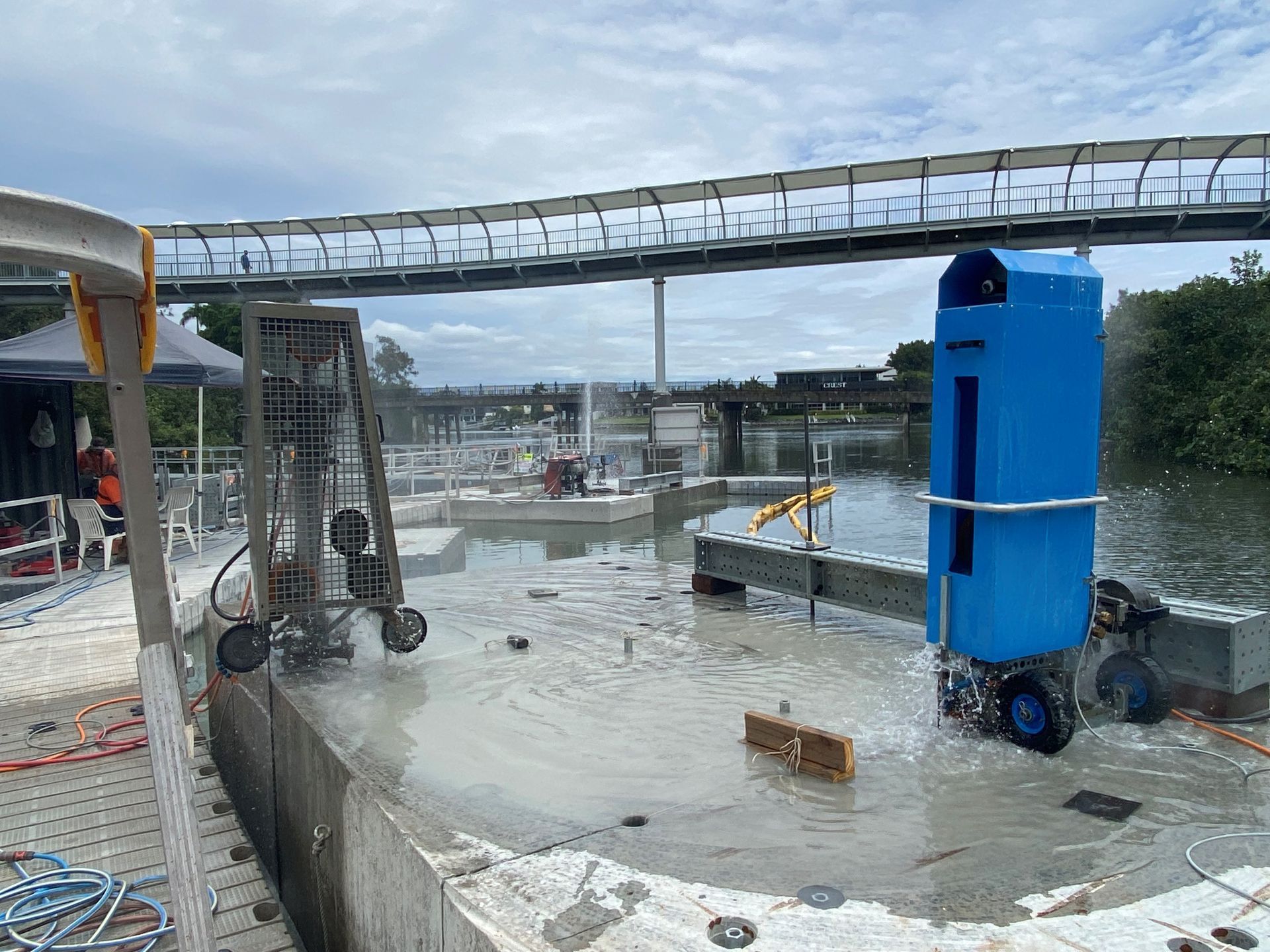 A blue container is sitting in the middle of a body of water next to a bridge.
