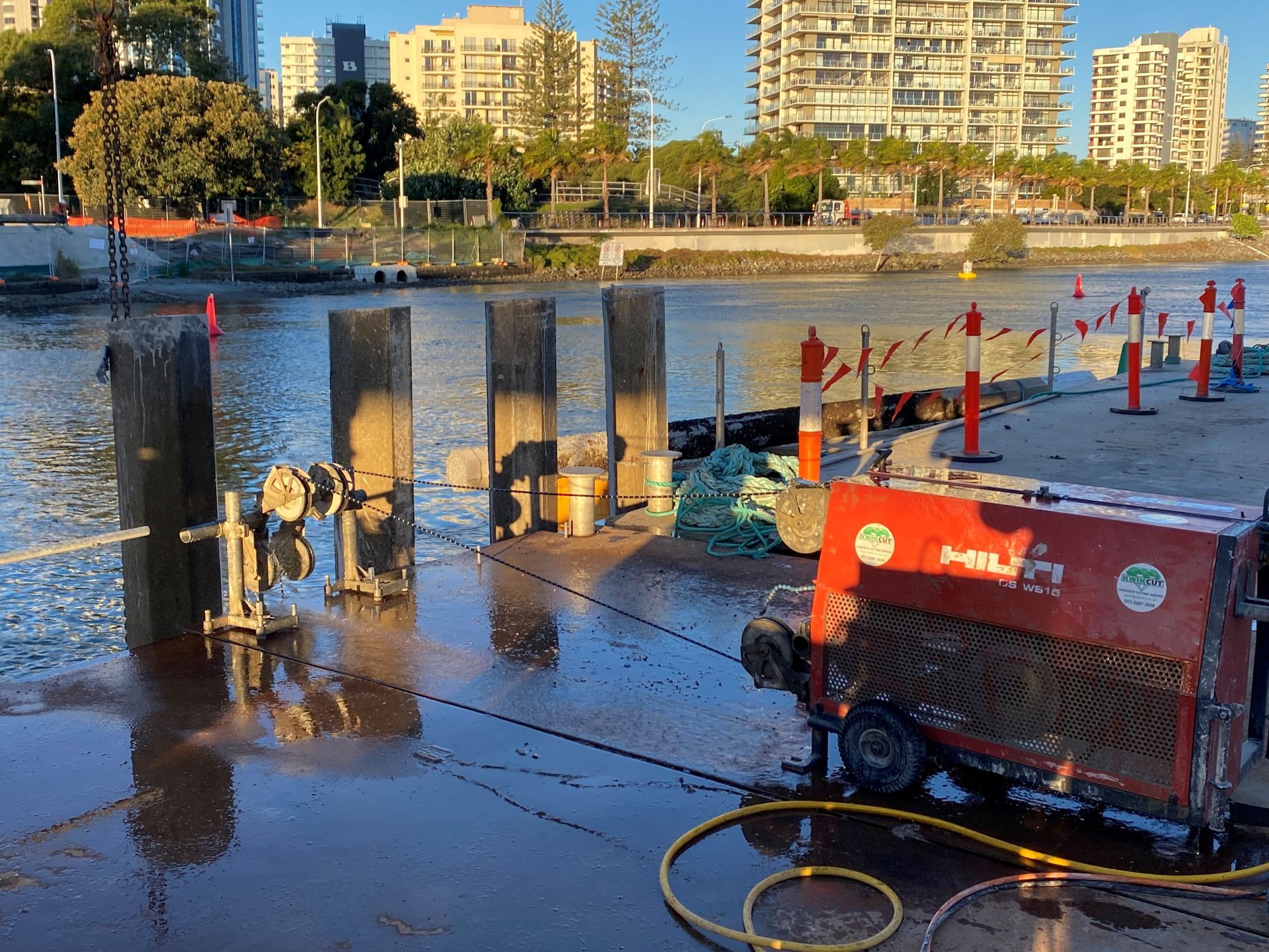 A red machine is sitting on a dock next to a body of water.