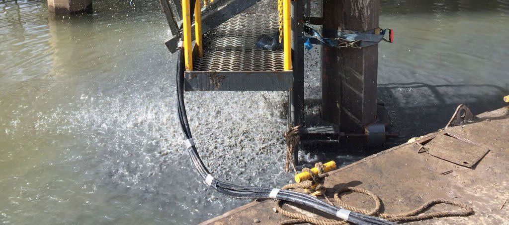 A machine is cutting a concrete wall next to a body of water.