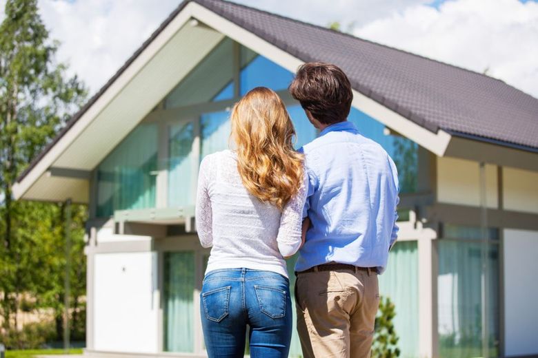 Couple standing outside a modern house, seen from behind, looking at the home