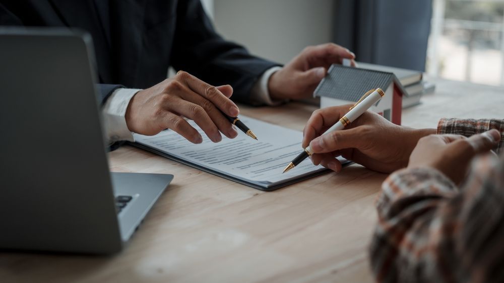 Hands working over a notebook at a desk with a laptop and smartphone in a meeting.