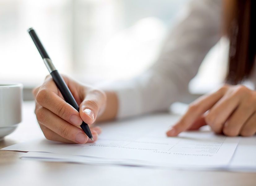 A woman is writing on a piece of paper with a pen.