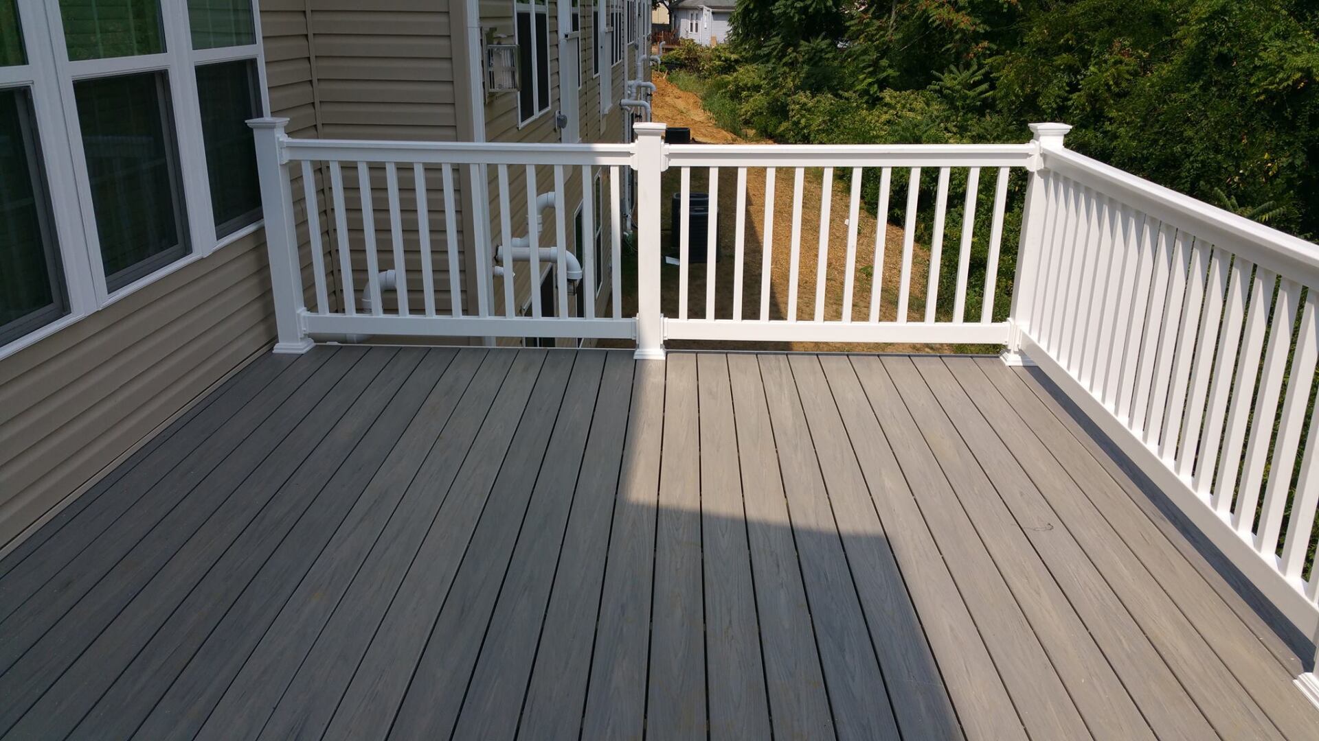 White wooden deck with railing beside a house, partly shaded by sunlight