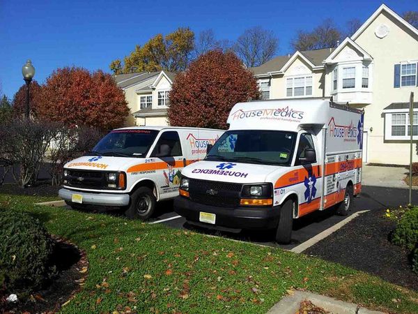 Two white-and-orange ambulances parked in front of houses on a sunny suburban street
