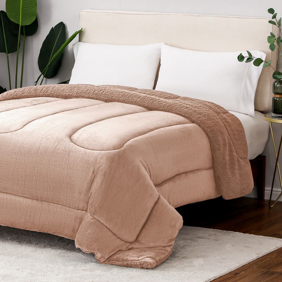 Edredón y almohadas beige sobre una cama con una manta marrón en un dormitorio luminoso.