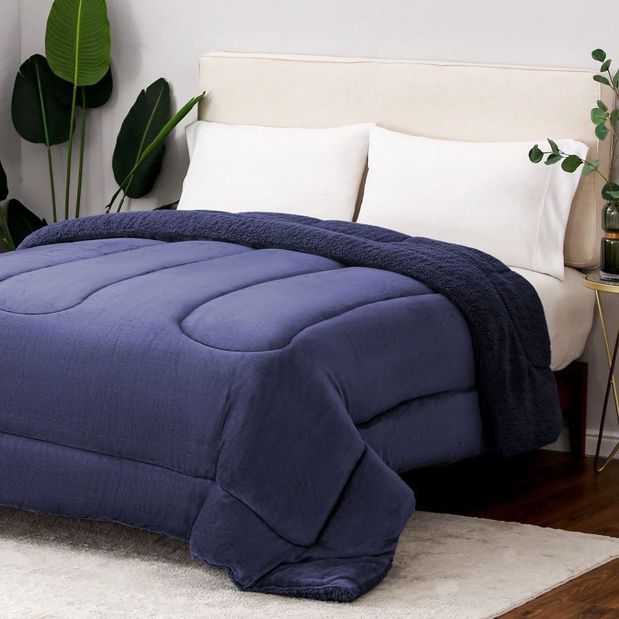 Edredón y almohadas beige sobre una cama con una manta marrón en un dormitorio luminoso.