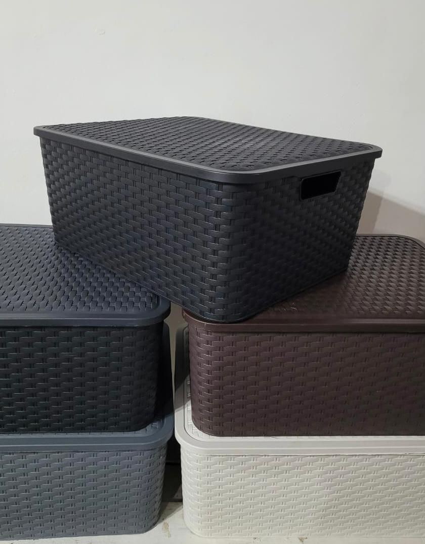 Cajas de almacenamiento tejidas apiladas en negro, marrón y blanco contra una pared lisa.
