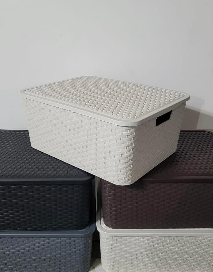 Cajas de almacenamiento tejidas apiladas en negro, marrón y blanco contra una pared lisa.