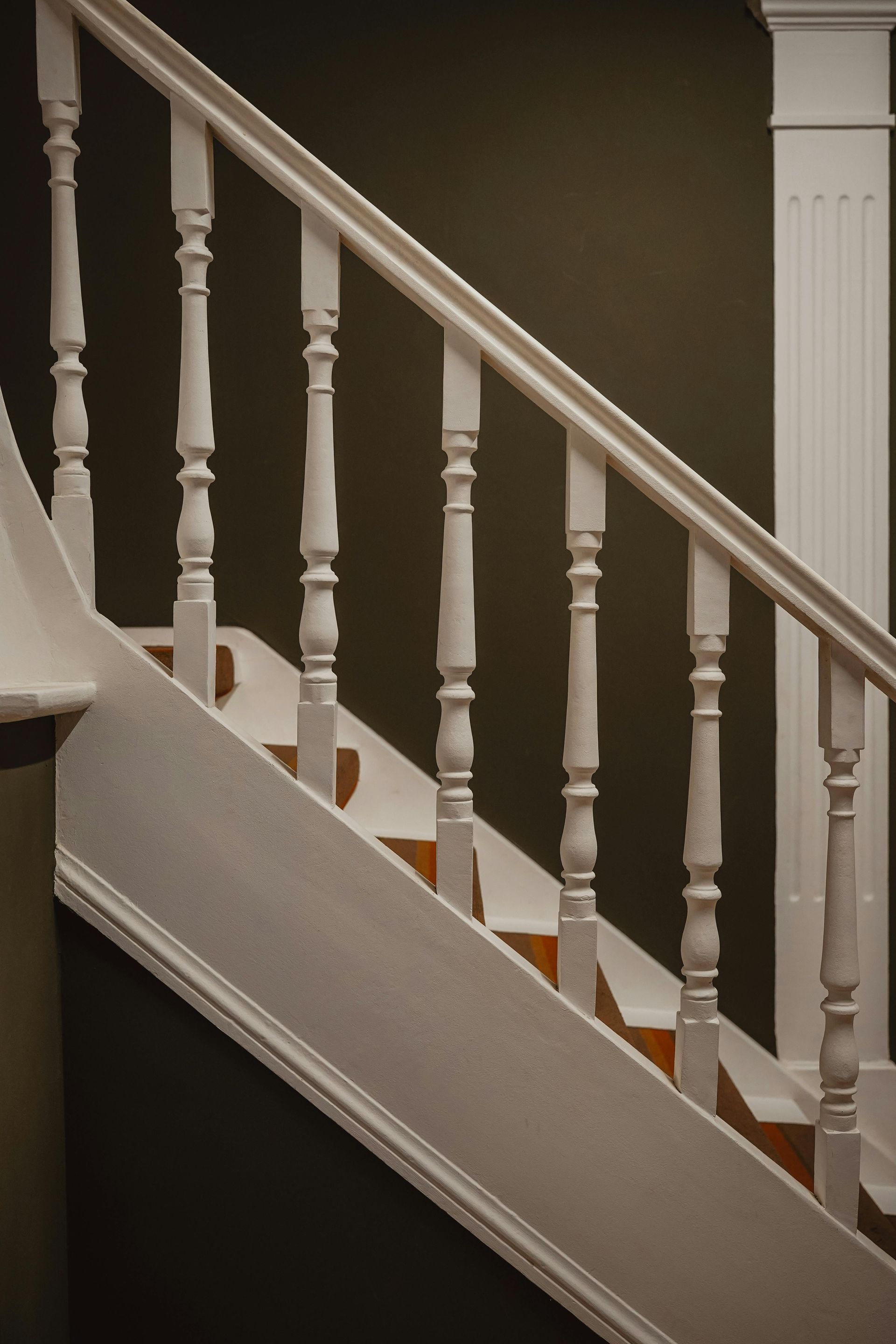Escalera de madera blanca con barandilla de balaustres contra una pared oscura.
