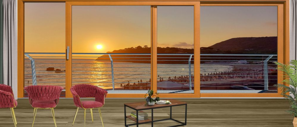 Vista del tramonto attraverso grandi finestre con sedie rosse e un tavolo su una terrazza affacciata sull'oceano