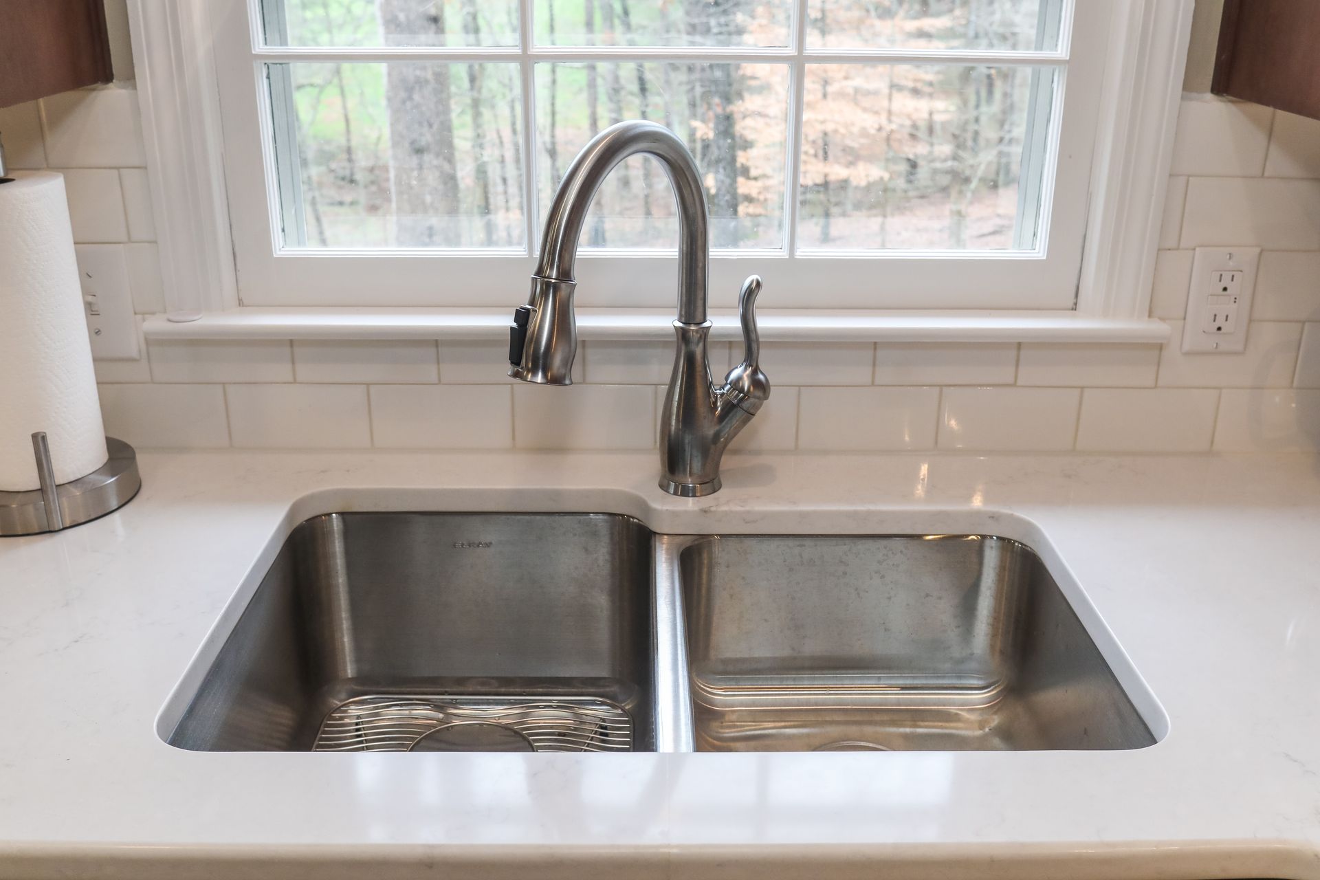 Stainless steel double kitchen sink under a window with a chrome faucet and soap dispenser