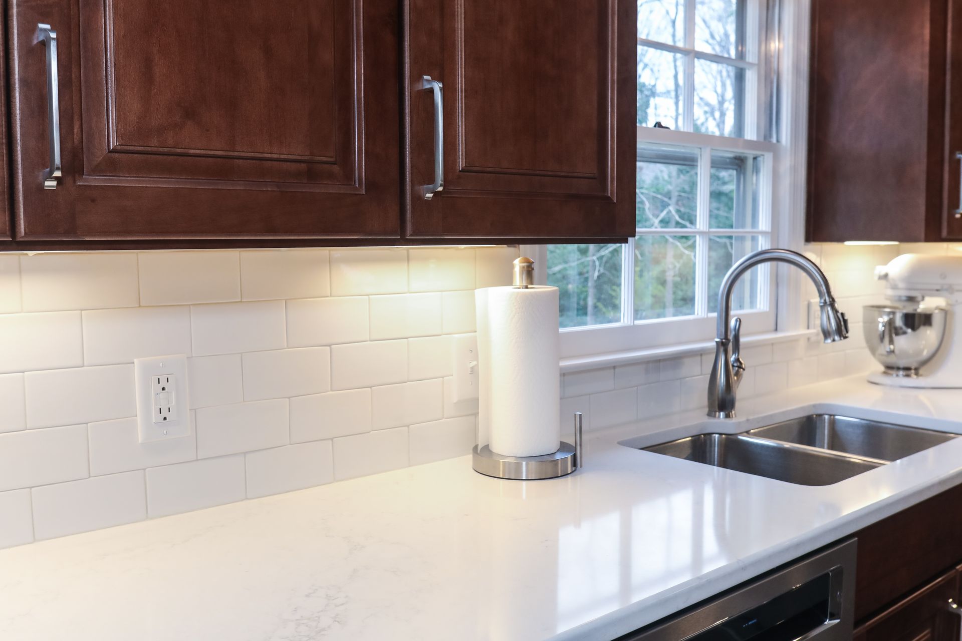 Modern kitchen with white countertop, dark wood cabinets, sink, and window above the faucet
