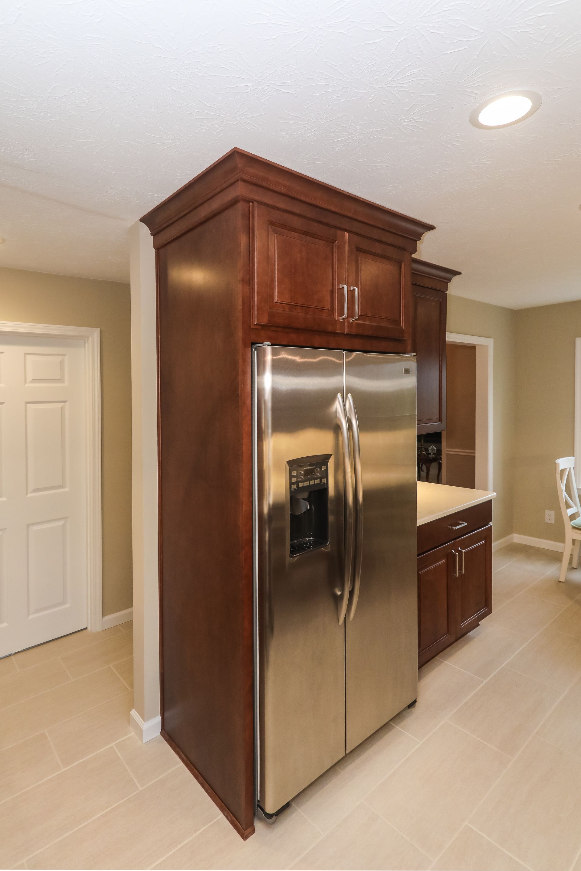 Kitchen with stainless steel refrigerator built into dark wood cabinetry and beige tile floor.