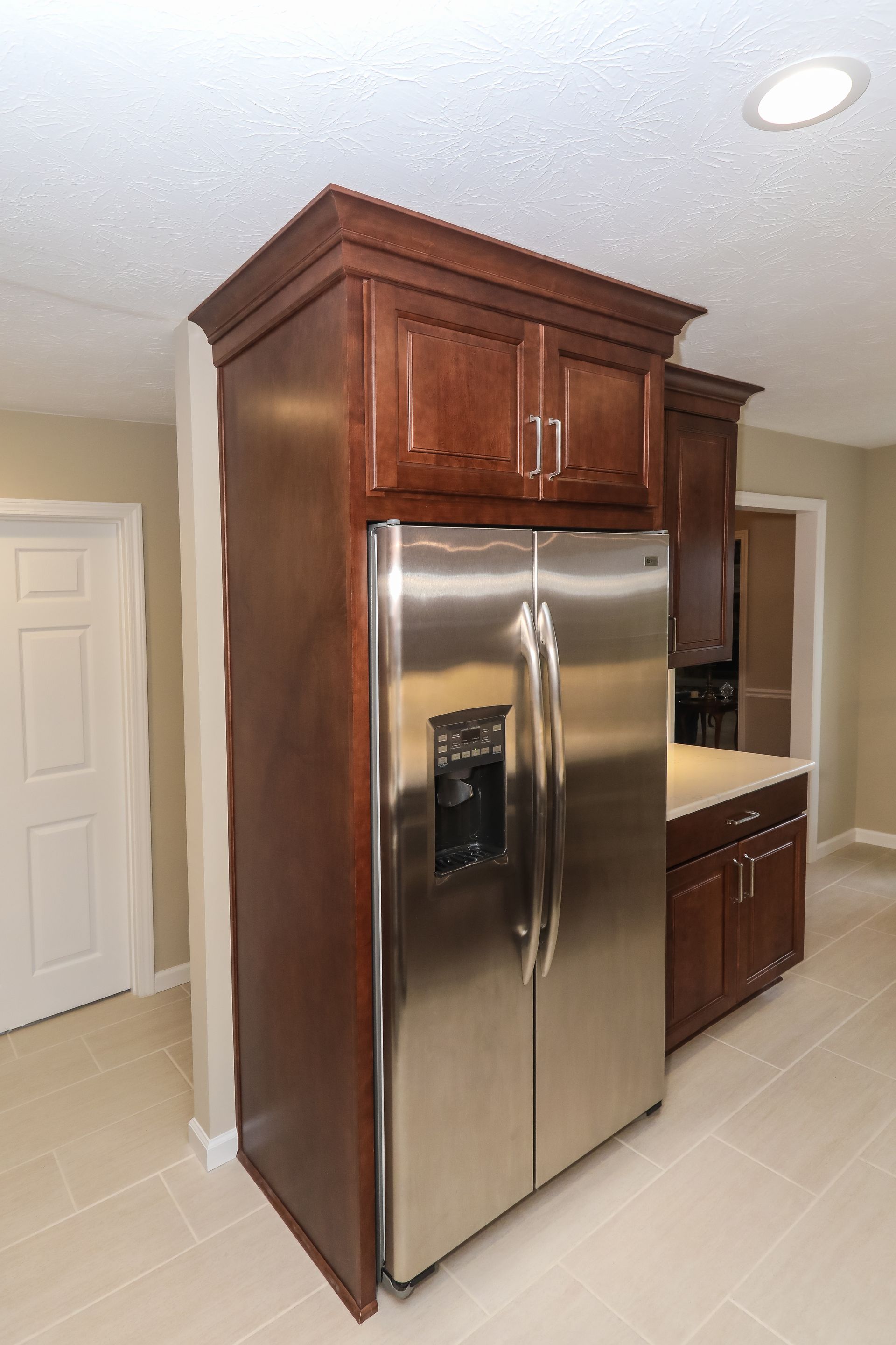 Kitchen with stainless steel refrigerator built into dark wood cabinetry and beige tile floor.