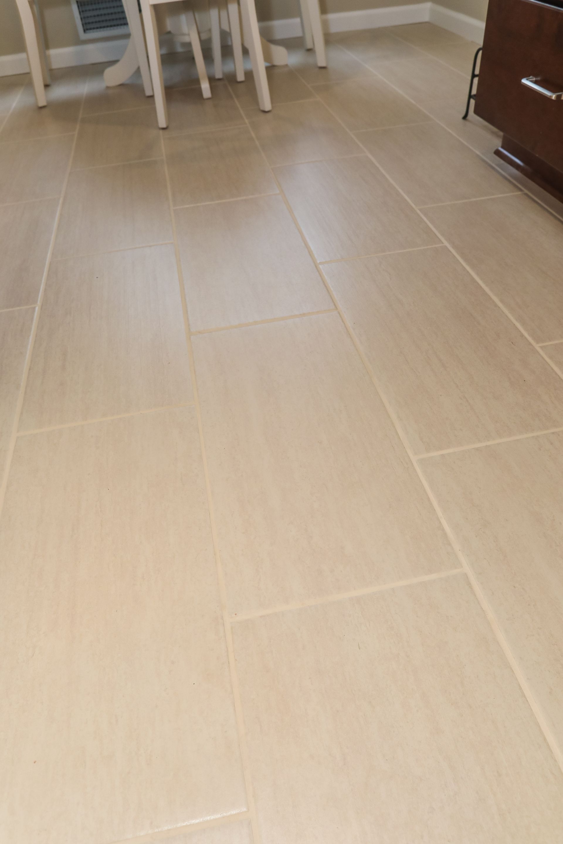 Light beige tiled floor in a room with a dining table and dark cabinet in the background