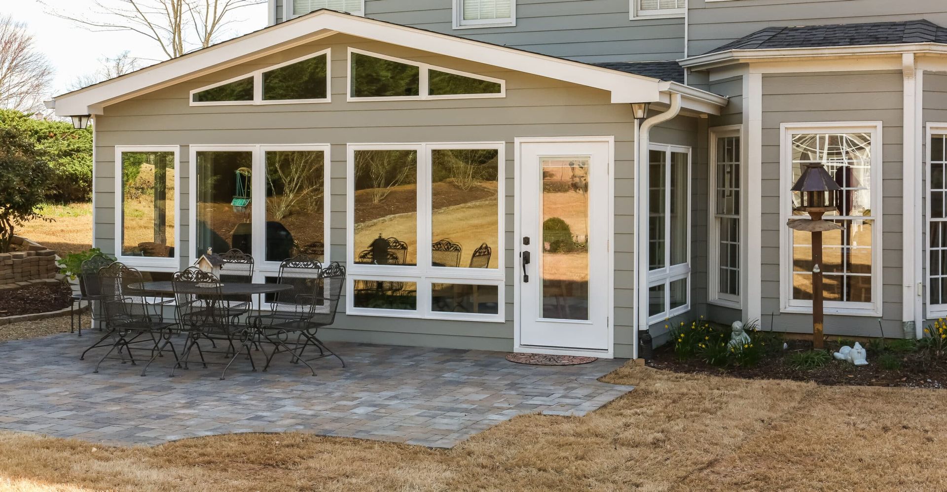 Sunroom with large windows, white trim, and outdoor patio furniture beside a house