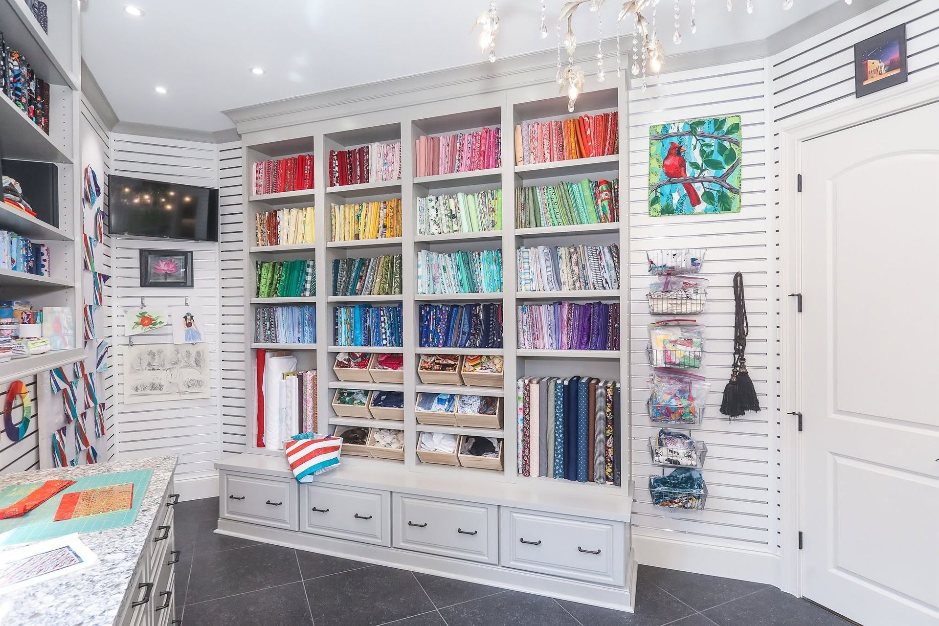 Bright craft room with rainbow fabric shelves, drawers, and sewing supplies on white walls.
