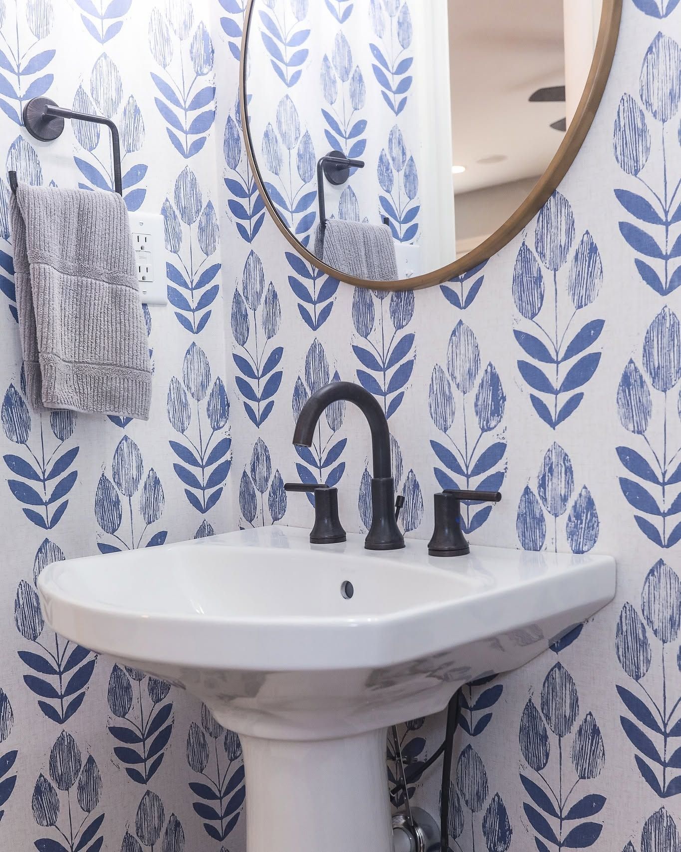 Bathroom sink with black faucet, round mirror, and blue leaf-pattern wallpaper