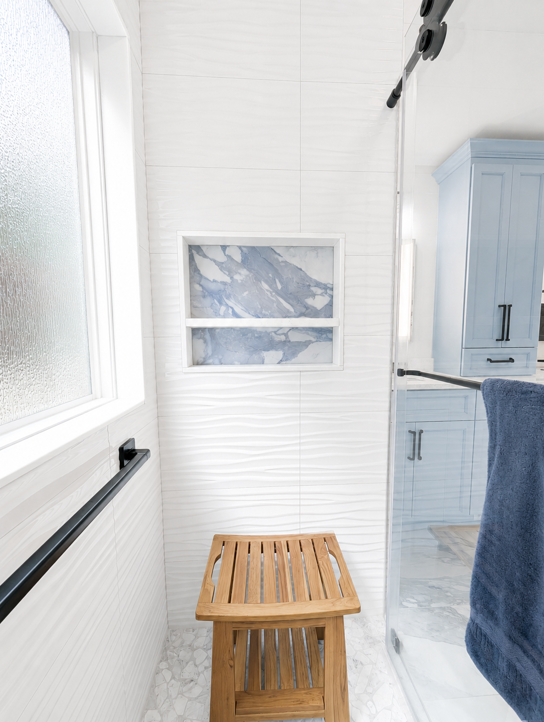 Bright bathroom with frosted window, blue cabinets, towel, and a small wooden stool in the center.