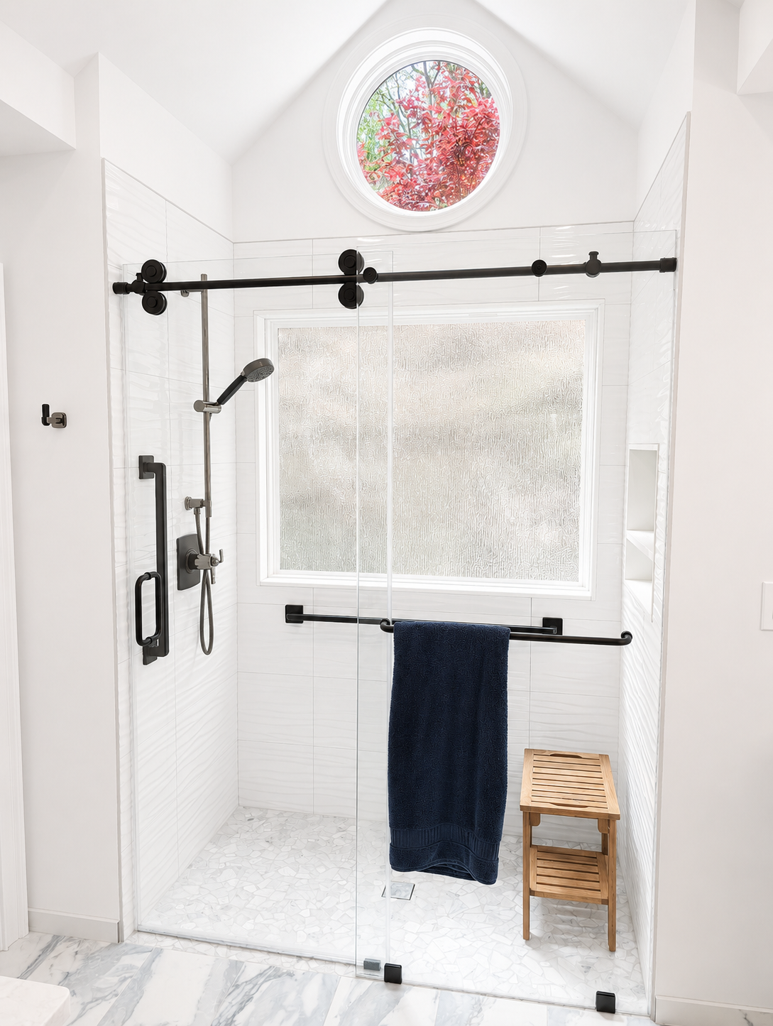 White tiled shower with black hardware, frosted window, round stained-glass vent, towel, and small stool