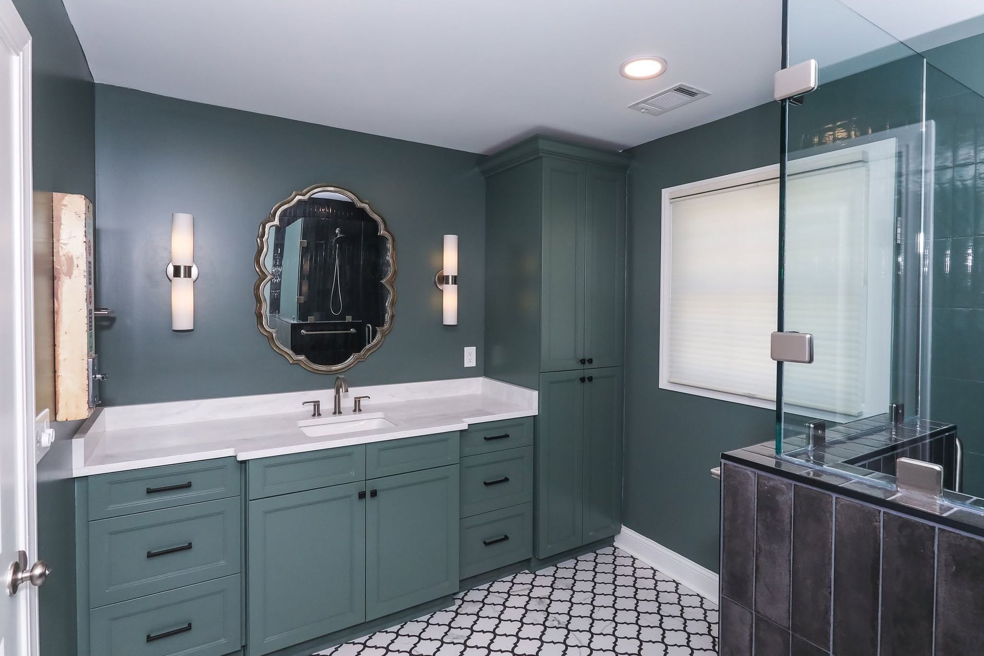 Teal bathroom with double vanity, oval mirror, wall sconces, and glass shower enclosure