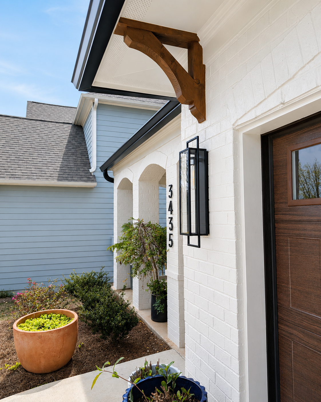 White stucco front porch with wooden awning, lantern light, potted plant, and dark wood door