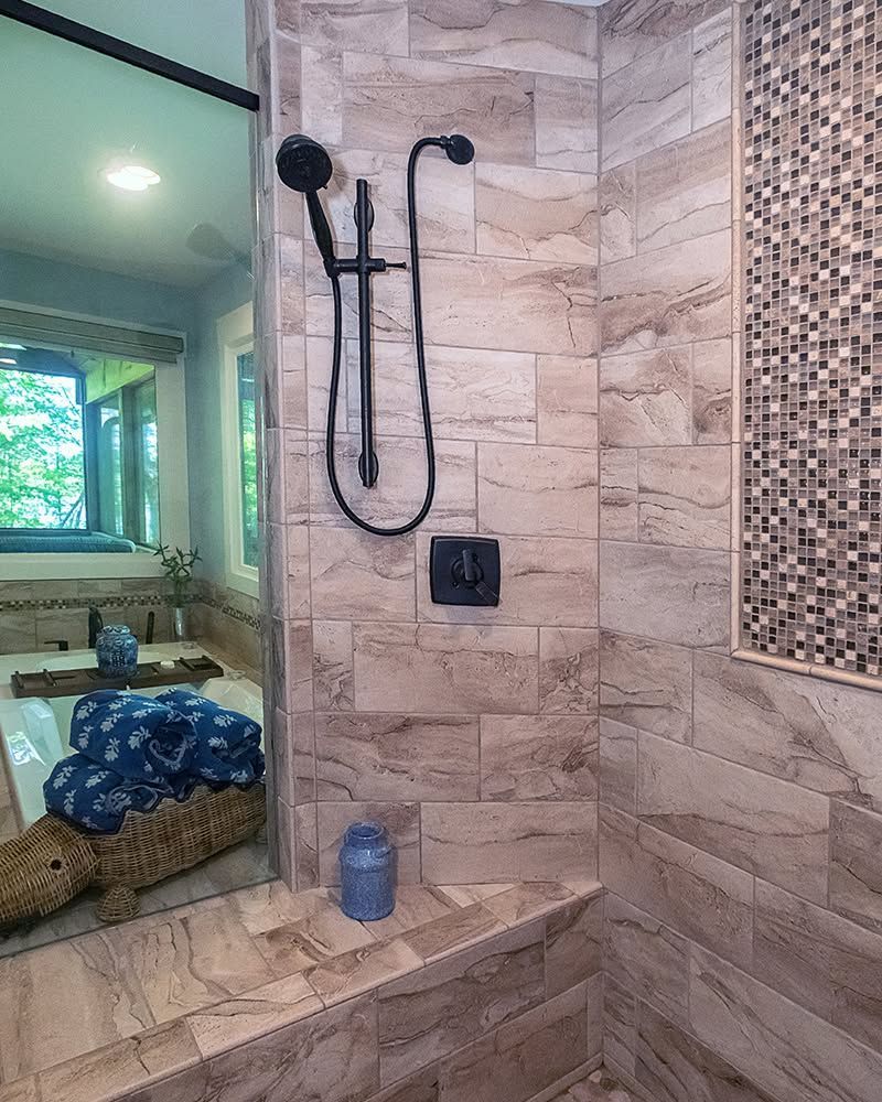 Tiled walk-in shower with black fixtures, bench, and mosaic accent wall beside a bedroom window.