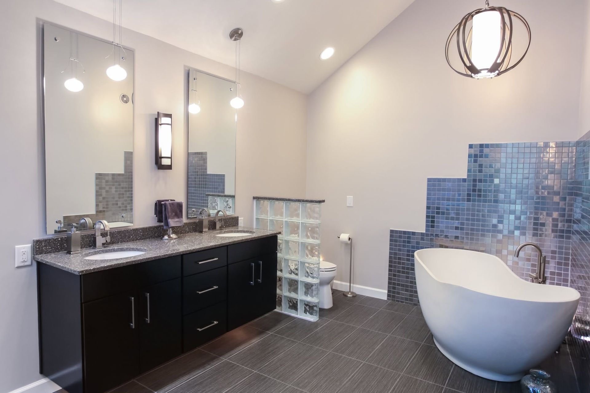 Modern bathroom with double vanity, large mirrors, blue tile accent wall, and a freestanding tub